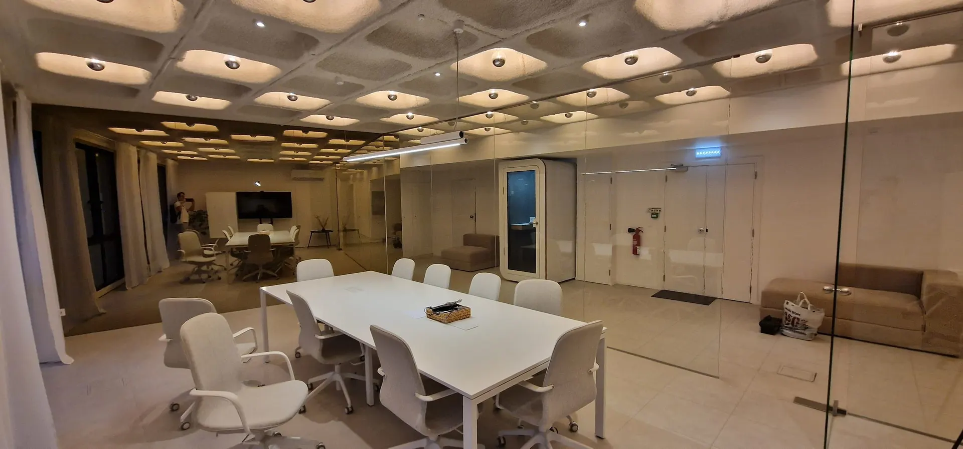A single-person Silentbox Solo booth standing beside a white meeting room with a long table and swivel chairs.